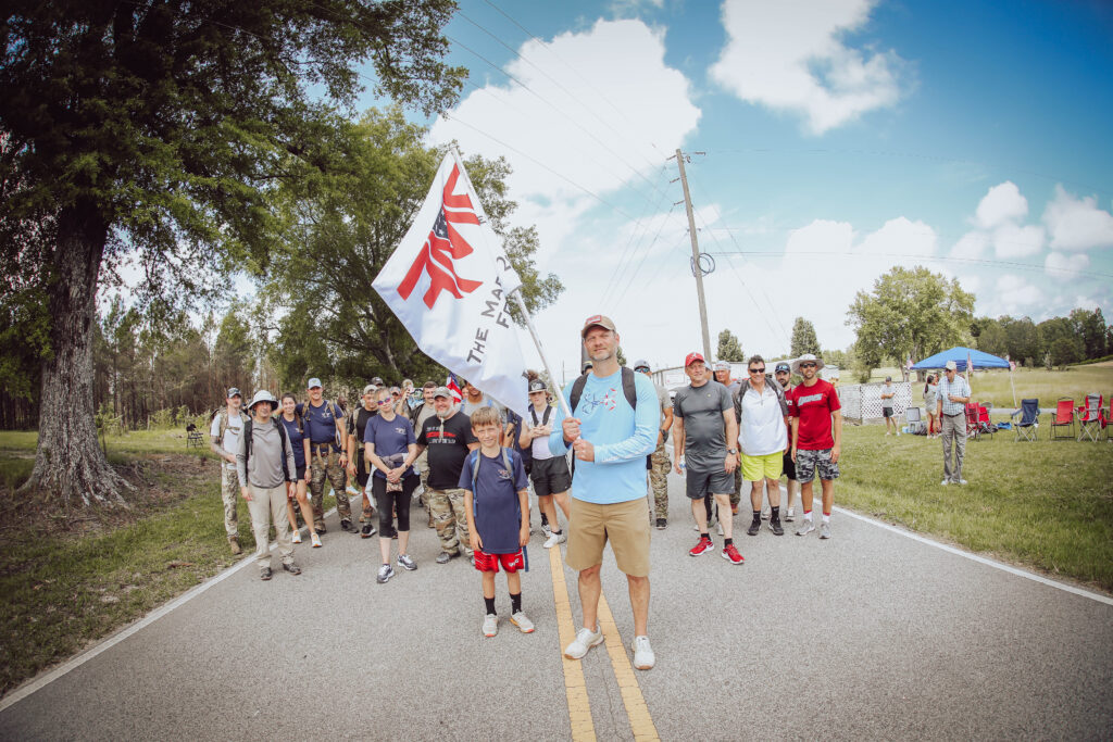 group of people rucking with weighted backpacks to honor SrA Mark Forester CCT