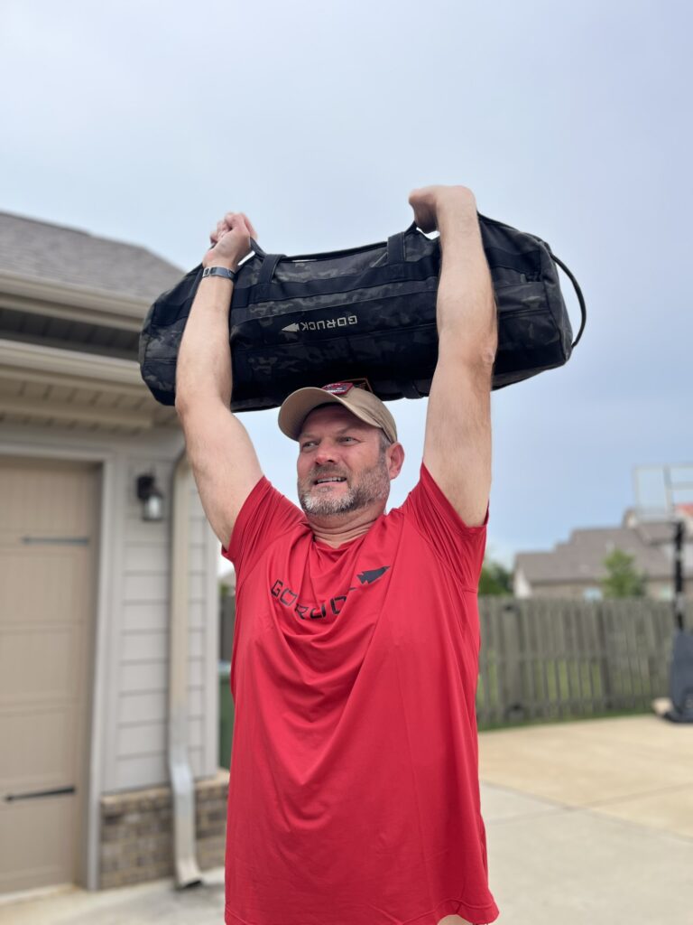 male in goruck toughmesh shirt lifting sandbag.