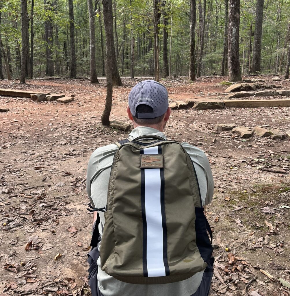 man sitting in woods with goruck basic rucker
